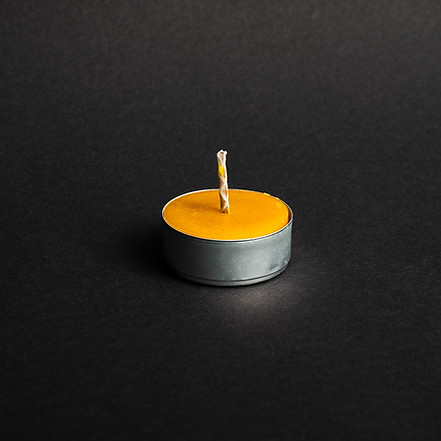 świeczka z naturalnego wosku pszczelego tealight w aluminium na czarnym tle