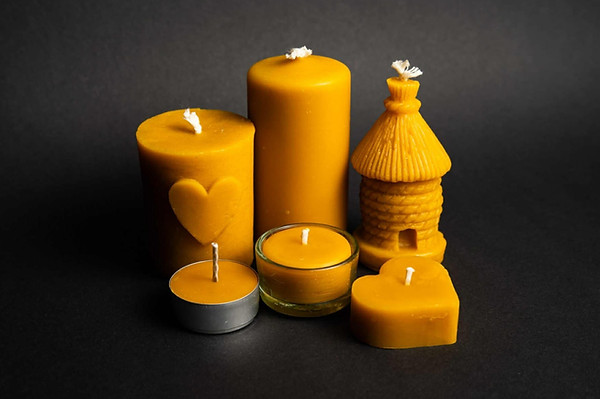 grupa świec z naturalnego wosku pszczelego: świeczka w kształcie walca z motywem serca, świeczka w kształcie walca, świeczka w ksztłacie ula, świeczka tealight w aluminium, świeczka tealight w szkle, świeczk w kształcie serca na czarnym tle