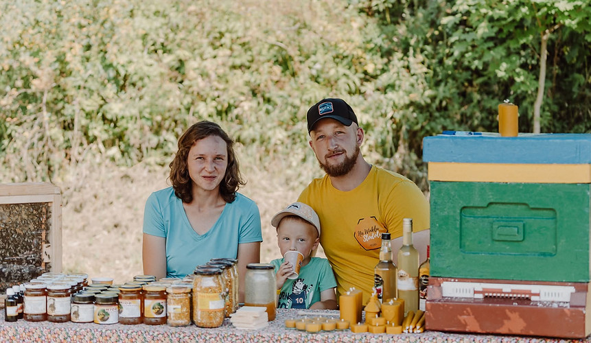 rodzinę na pikniku, stół z ramką z pszczołami za szkłem, produkty z pasieki, ul; w tle rośliny