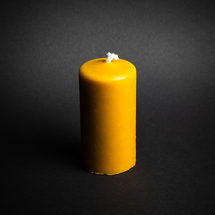 świeczka z naturalneg wosku pszczelego o kształcie walca na czarnym tle