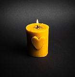 świeczka z naturalnego wosku pszczelego o kształcie walca z motywem serca, zapalona, na czarnym tle