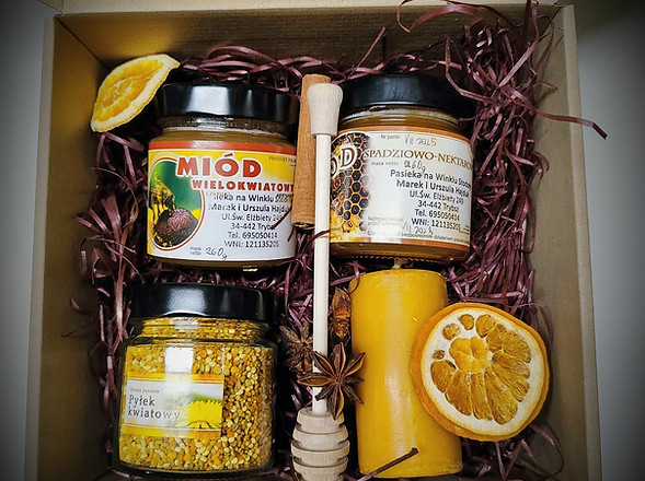 środek zestawu prezentowego zawierający: miód wielokwiatowy, miód spadziowo-nektarowy, pyłek kwiatowy, świece z naturalnego wosku pszczelego z kształcie walca, nabierak do miodu, dodatki dekoracyjne: pomarańcza plastry suszone dwie sztuki, gwiazki anyżu trzy sztuki, laska cynamonu