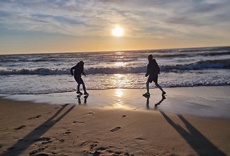 The image shows two children playing on a beach at sunset and at Wanderwood Coaching near Winchcombe, Cheltenham, Emilie offers coaching sessions online or in person to adults who may be wanting to make changes in relation to their families or parenting, whether it be in relation to blended families, single parents or challenges such as work life balance or co-parenting.