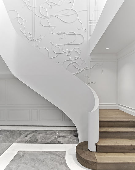 White ribbon staircase with oak steps. The space has luxury finishes such as stone floors and wainscoting, as well as a custom wall installation.