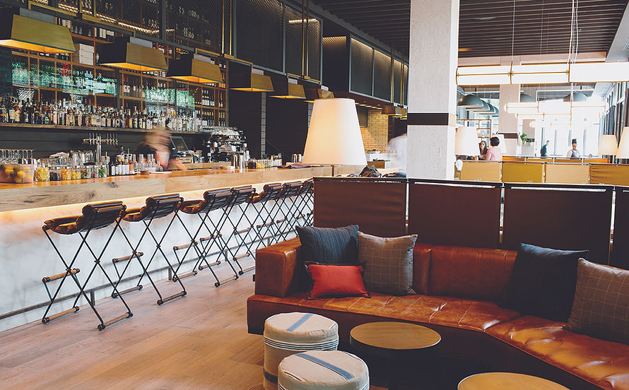 Waiting area near the bar in an Atlanta restaurant. The waiting area features lounge-style seating upholstered in leather that matches the barstools, as well as ample pillows and poufs.