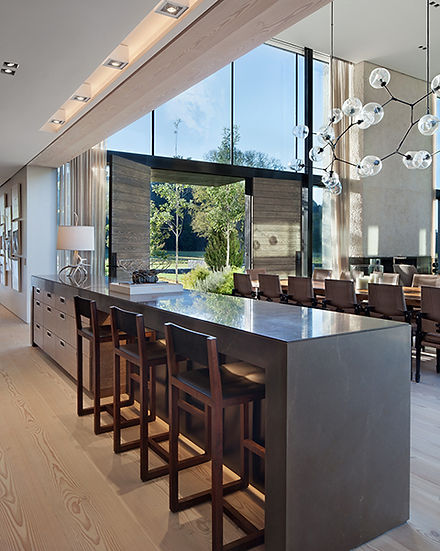 Kitchen island seating in a new construction Nashville home designed by Liz Curry Studio. The seating faces the entryway with double doors and panoramic windows. The waterfall island is high gloss, and the cabinetry is a medium tone wood.