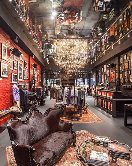 John Varvatos retail store interior featuring the custom mirrored ceiling and bold red brick walls with the seating area custom chandelier sculpture centering the space