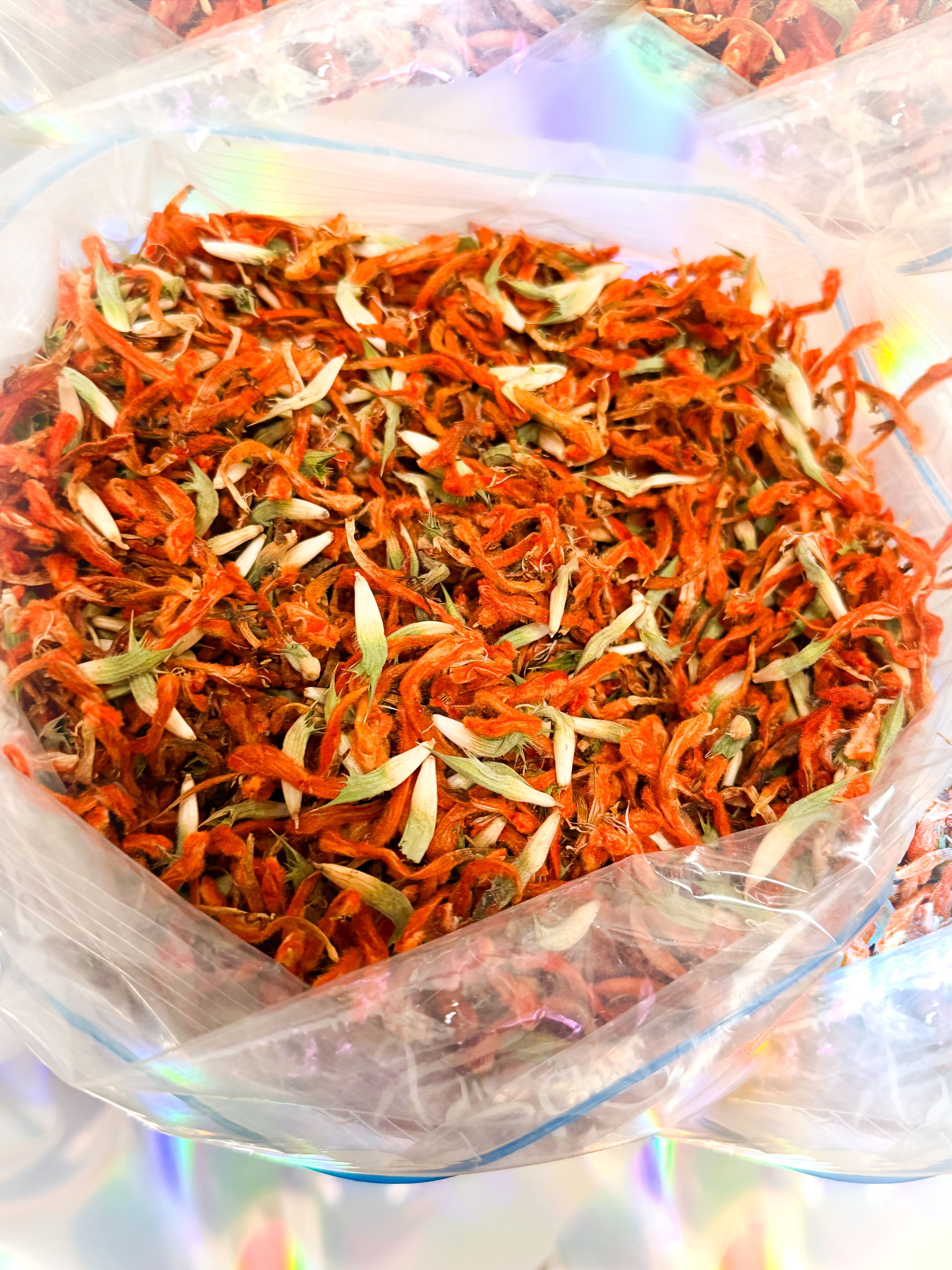 A close-up of dried orange flower petals mixed with green leaves inside a clear plastic bag