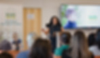 New Mexico State Treasurer Laura M. Montoya stands strong at a podium explaining the benefits of the Baby Bonds program to a group of people listening intently.