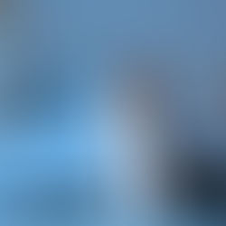 Woman in pajamas sits on a bed looking pensive. Blue and white bedroom with a lamp and shelf in the background. Dimly lit mood.