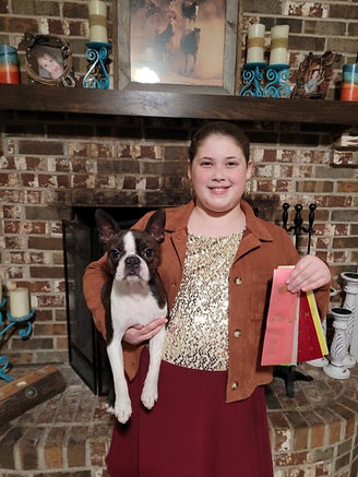 Young girl with Boston Terrier, holding ribbons, and smiling at the camera.