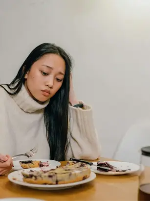 Mulher adulta com seletividade alimentar fazendo expressão pensativa olha para um prato de torta.