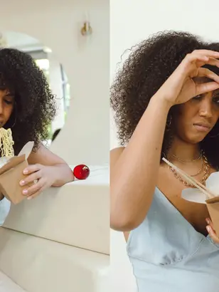 Mulher com seletividade alimentar de vestido azul come macarrão de caixa de delivery em quarto claro, com expressão de desagrado.