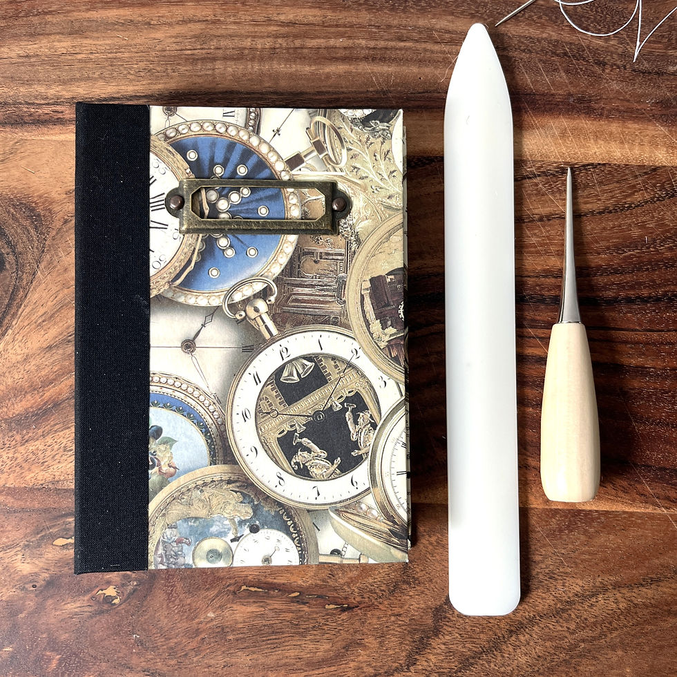 Thumbnail: A6 Book with vintage pocket watch design next to a bone folder and awl.