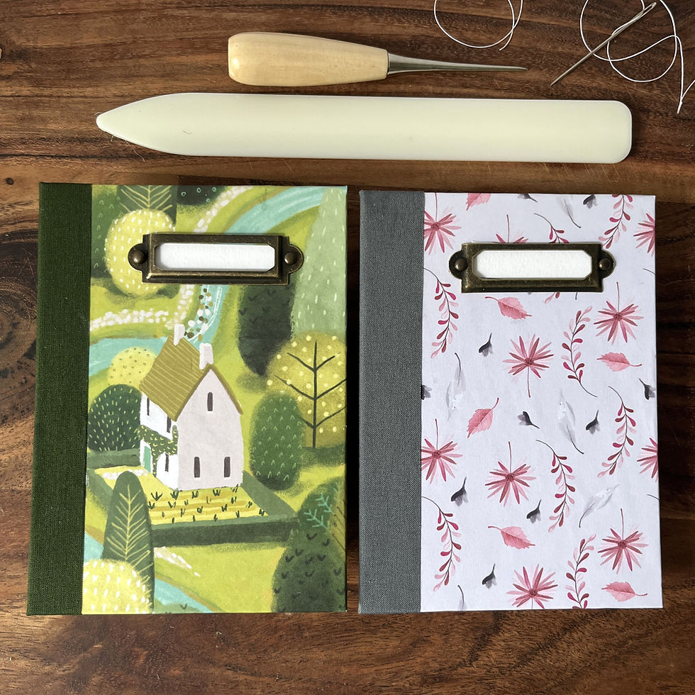 Two A6 handmade books next to a bone folder, needle and awl