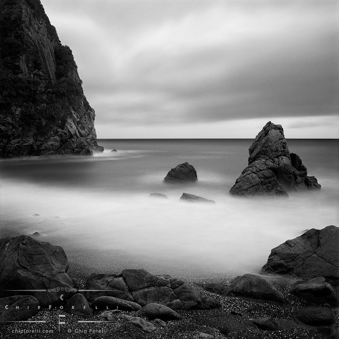 A time exposure of a rocky shoreline showing the surf and sky smoothed out into creamy tones of white and grey.