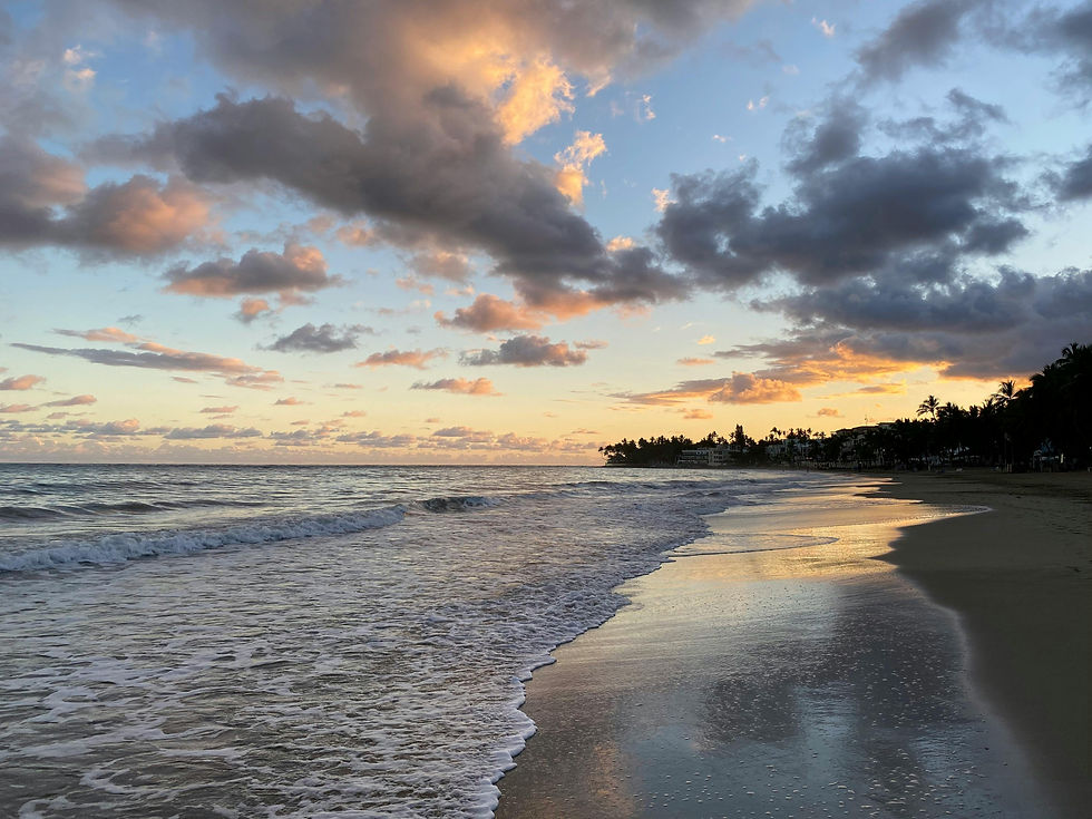 Sunset over a tranquil beach with colorful clouds, reflected on the wet sand. Waves gently wash ashore, creating a serene atmosphere.
