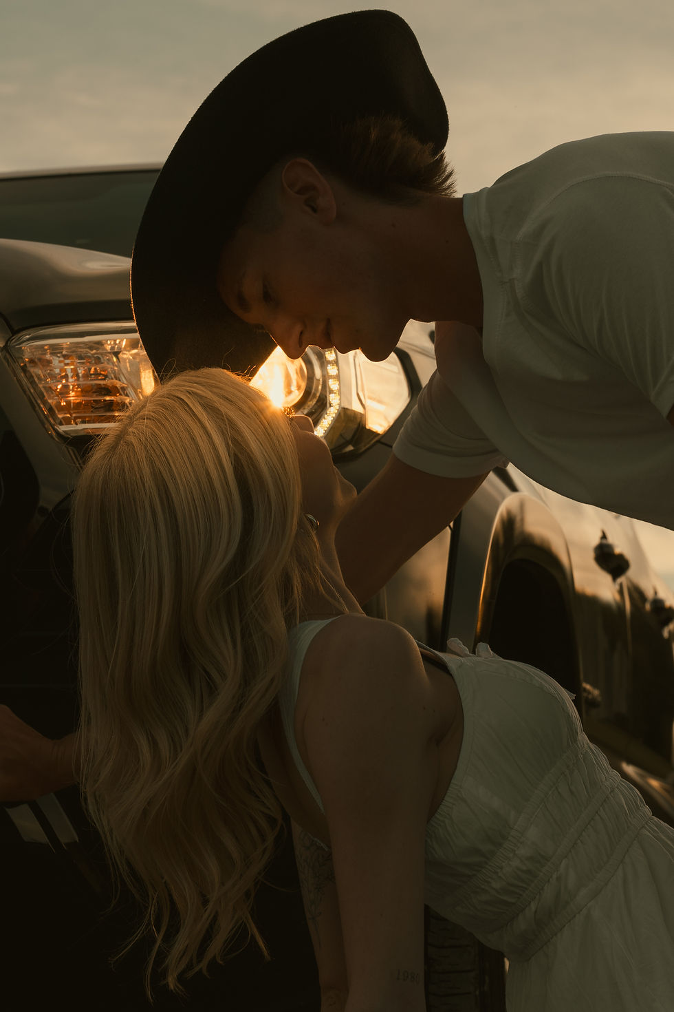 Country-western couple at dusk lit up by the headlights of their old pickup truck