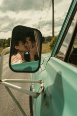Couple seen leaning in for a kiss through the side mirror of a vintage truck