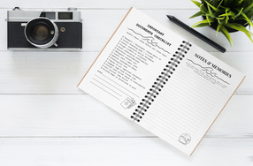 Open Print & Panic Cruise Journal showing black and white sea day and notes pages with a camera, pen, and plant on a white desk