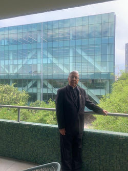 El padre Humberto en Aulas II, con la Biblioteca al fondo
