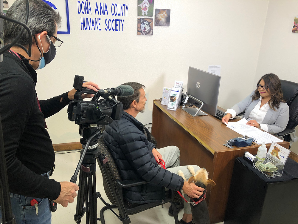 A man films the Director of the Doña Ana Humane Society talking at her desk.