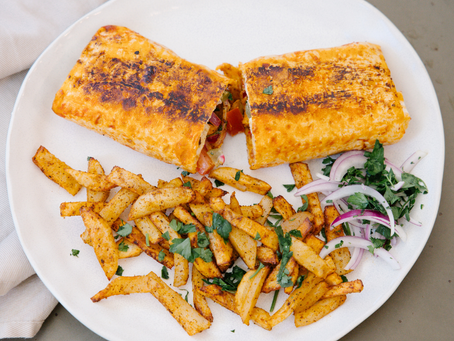 Golden chicken shawarma halved and served with perfectly seasoned fries and fresh red onion on a white plate.