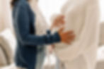 Model stands face to face with pregnant model, each holding the pregnant woman's belly.