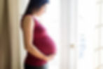 Pregnant woman standing next to a well lit window with hands below her belly