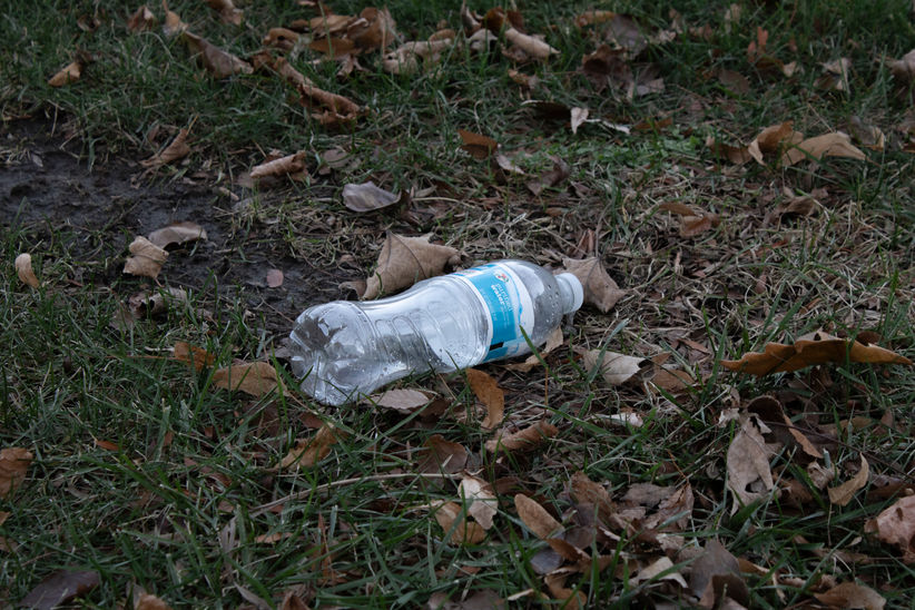 A photograph of water bottle on ground with dead leaves. 