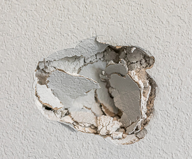 A hole in the wall of a hallways caused by a fist punching through the wall.jpg