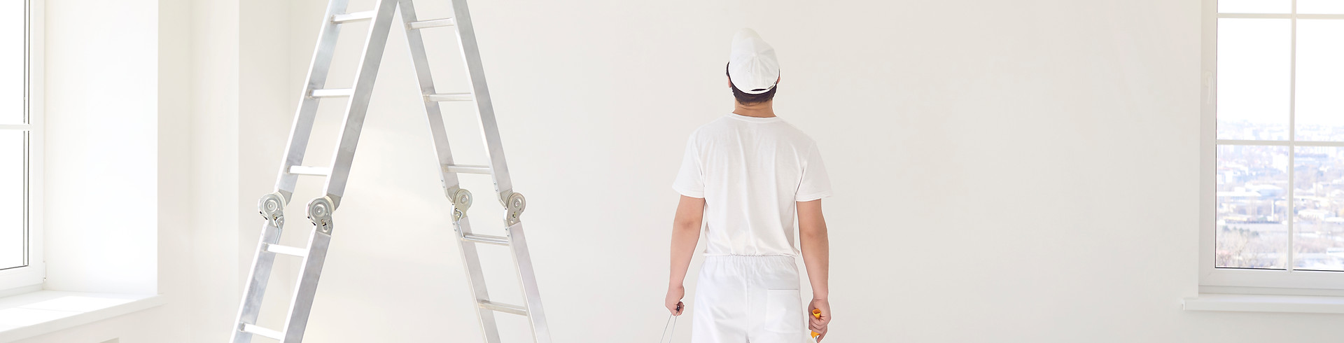 A male painter in a white uniform with a roller works in his hand in a white room.jpg