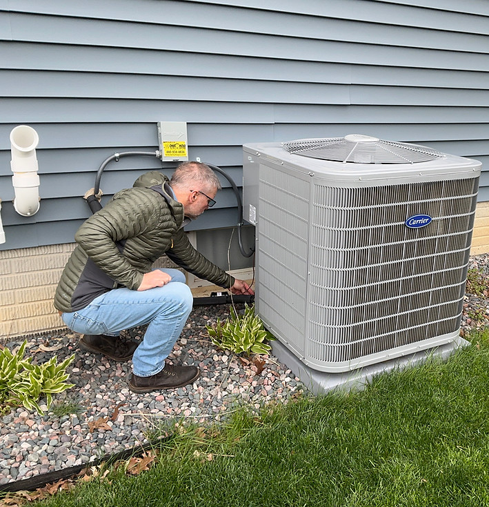 Technician inspecting an outdoor AC unit beside a house.