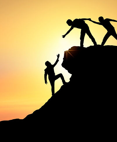 Silhouetted figures helping each other climb a rocky peak against a sunset backdrop.