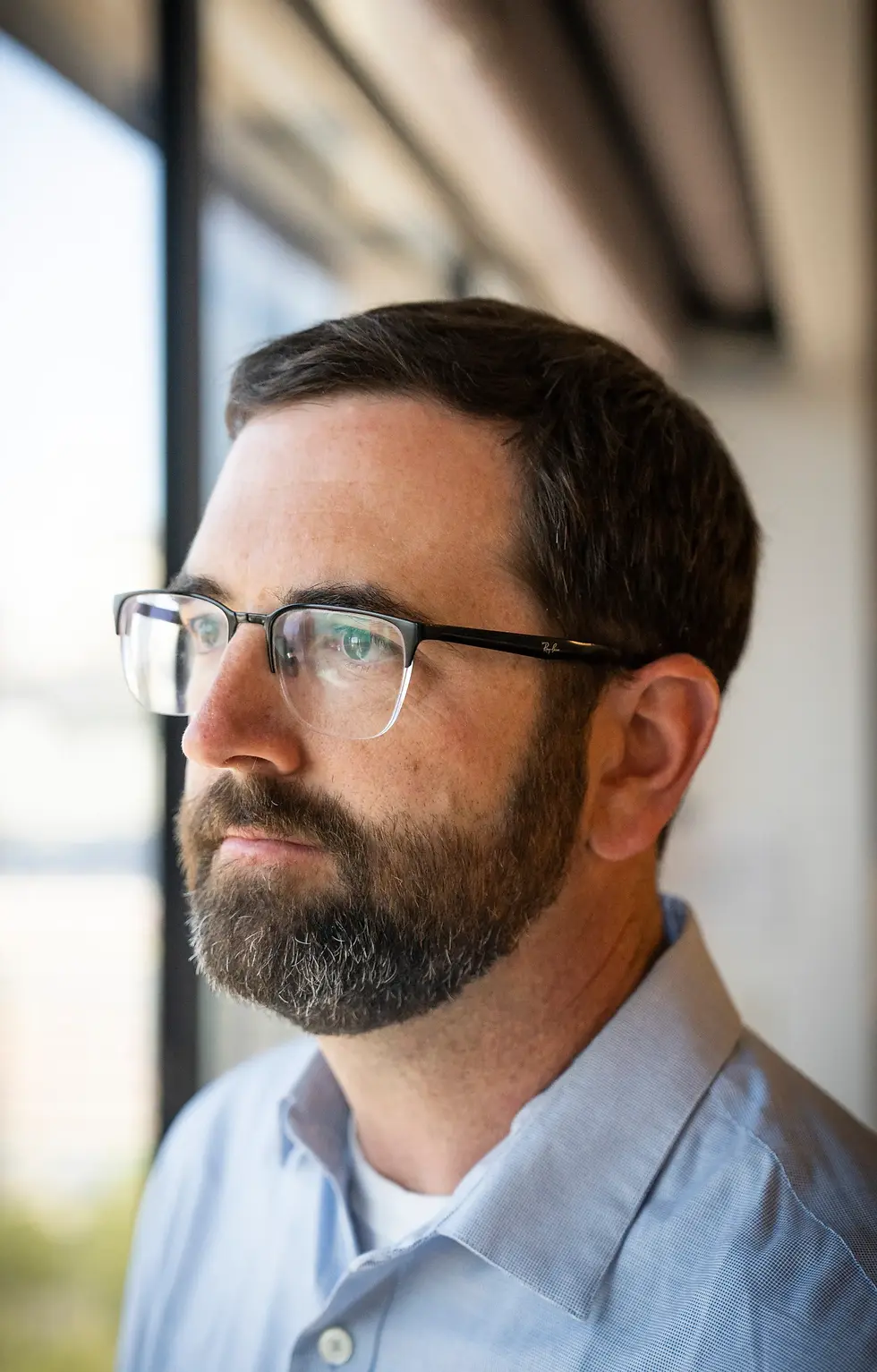 Brandon Cox looks thoughtfully out a window in an office setting.