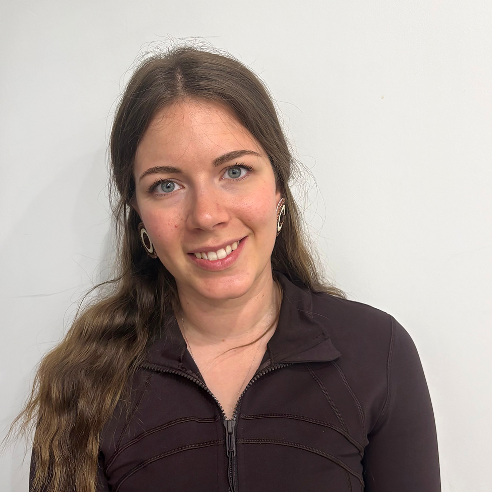 Smiling woman with long brown hair and blue eyes in a dark zip-up top, posed against a plain white wall.