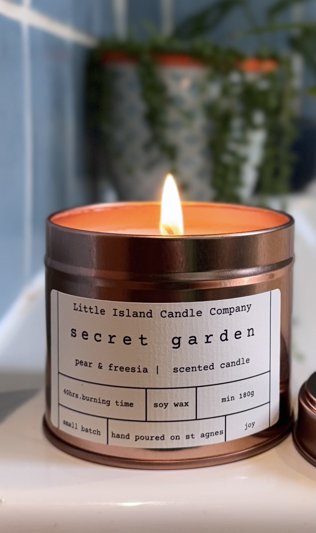 Secret Garden candle, lit, in a rose gold tin