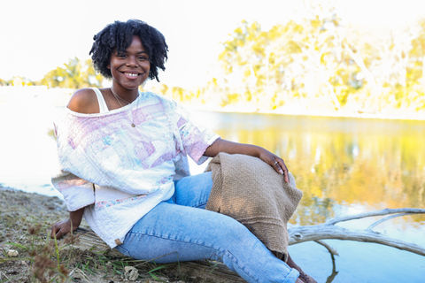A woman in an off the shoulder quilt top sitting on grass.