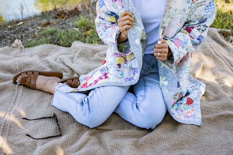 A woman sitting on a blanket wearing a quilt jacket.