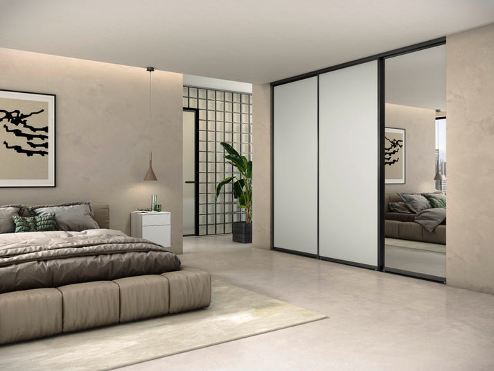 Bedroom wardrobe with light sliding doors, black frames and a full-height mirrored panel.