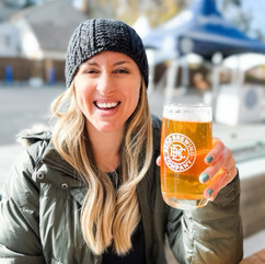 Girl in winter clothes holding up craft beer and Bend Brewing Company. 
