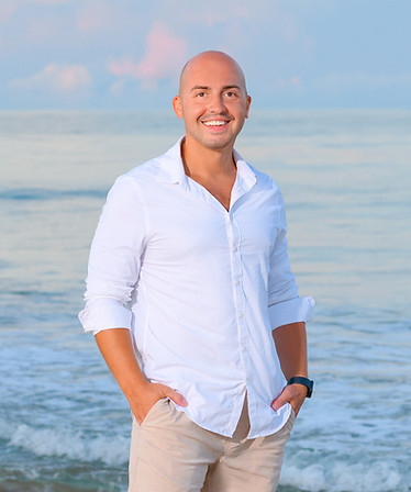 A photograph of Benjamin Horvat wearing a white shirt and khaki pants standing in front of the ocean.