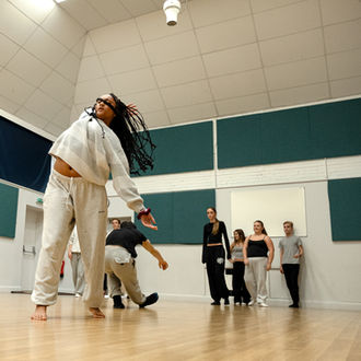 A dancer performs in a studio with others, wearing white, dancing together.