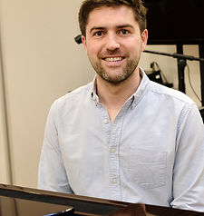 music teacher sitting at piano with audio visual equipment behind him