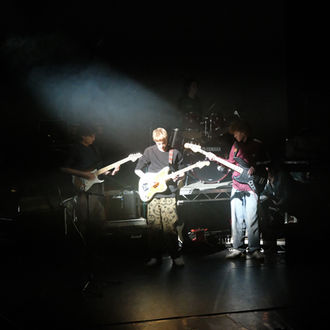 Band performing live on stage with guitars and a keyboard setup.