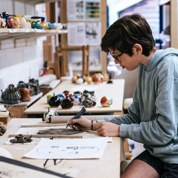 Young artist sketching details on pottery in a well-lit art studio.