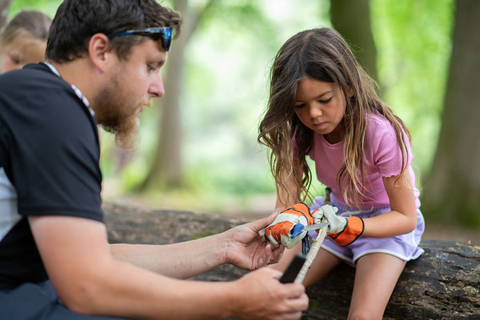 Teacher and girl whittling outdoors in a forest background