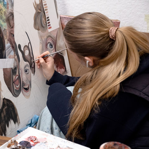 student painting on canvas with multiple faces and expressions, in progress