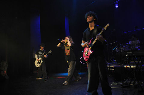 Band performing live on stage with guitars and a vocalist in action.