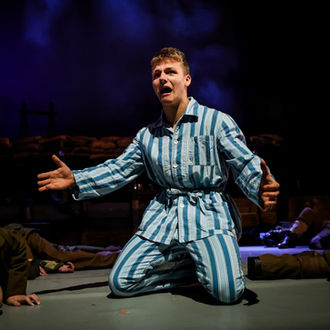 Actor kneels and gestures dramatically, wearing striped pajamas, stage play performance.
